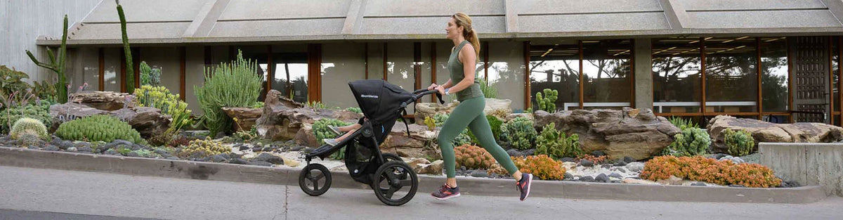 A woman jogging on a sidewalk, pushing a Bumbleride jogging stroller 