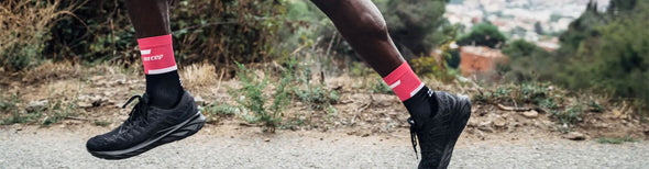 Man running along a hilltop road in pink and black CEP 4.0 mid cut compression socks and black running shoes.
