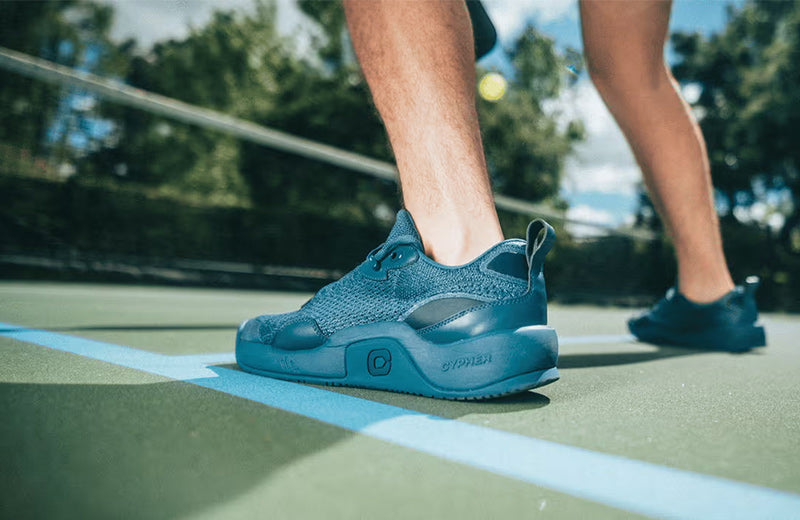 Lifestyle image: A pickleball player wearing Cypher Pickleball Key211 shoes on a green court.