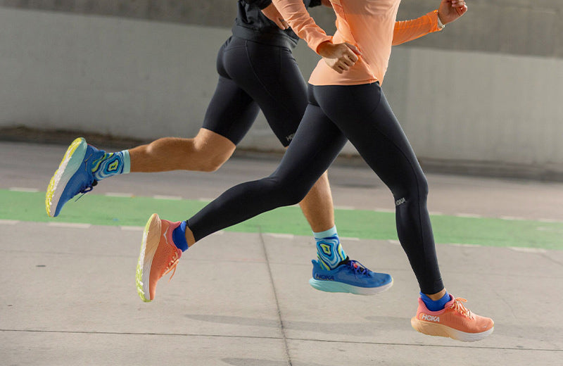 Lifestyle image: a woman and a man running on sidewalk in HOKA Arahi 7 running shoes.