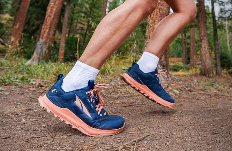 Lifestyle image: A person running a wooded trail in Altra Lone Peak 8 Women's Navy/Coral trail running shoes.