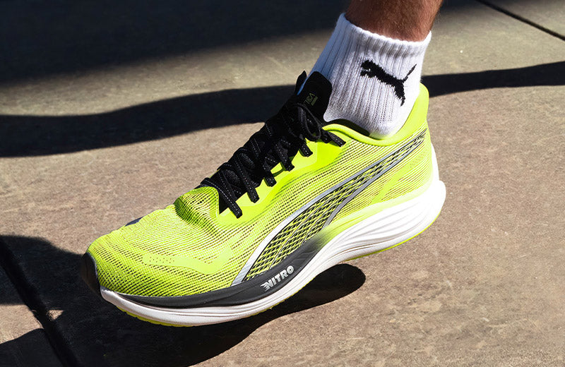 Lifestyle image: Closeup of a person running on a sidewalk in lime colored Puma Velocity Nitro 3 running shoes