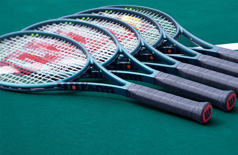 Wilson Blade v9 tennis racquets laying on a green tennis court.