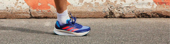Closeup of a man running in blue, red and white adidas adizero Boston 10 running shoes on gray pavement.