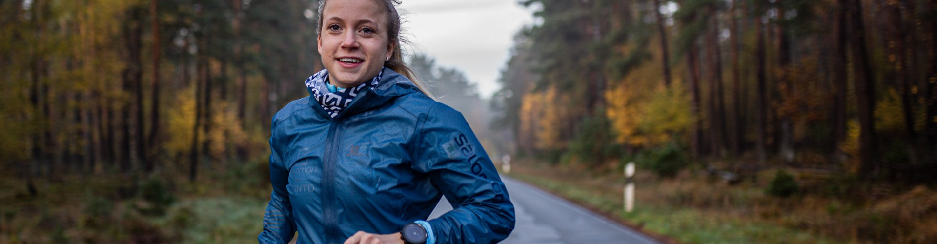 Woman on road surrounded by forest in Salomon running gear