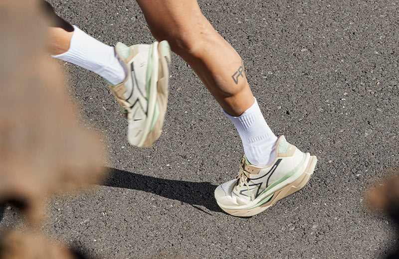 Lifestyle image: a person running on a paved road in Diadora Atomo v7000 2 Men's Whisper White/Irish Cream running shoes.