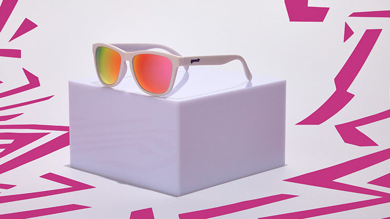 goodr OG Neon is My Neutral Sunglasses with red-tinted lenses on a white box against a pink geometric pattern