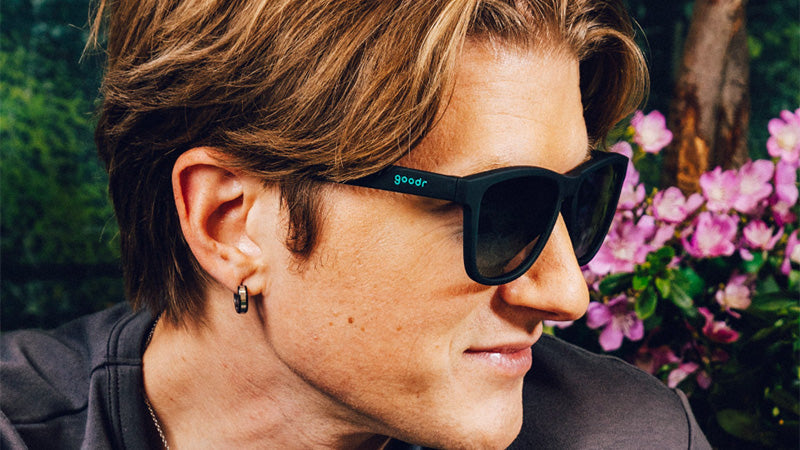 smiling woman weraing goodr howling at the neon moon bfg sunglasses on a green background