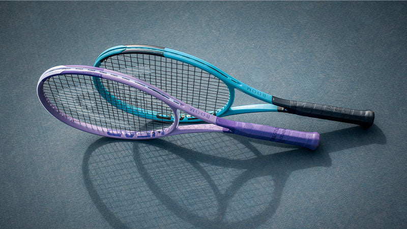 Purple and blue HEAD Boom 2026 tennis racquets posed on a light blue tennis court surface