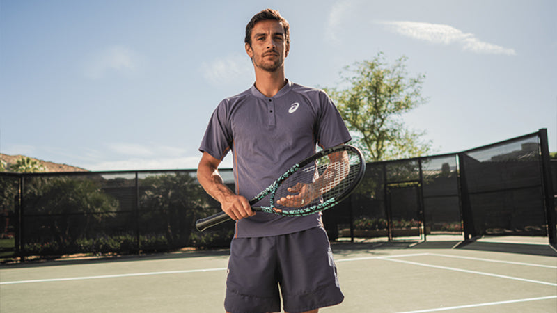 Man holding a HEAD Boom Neon New York Limited-Edition tennis racquet on a tennis court with trees in the background