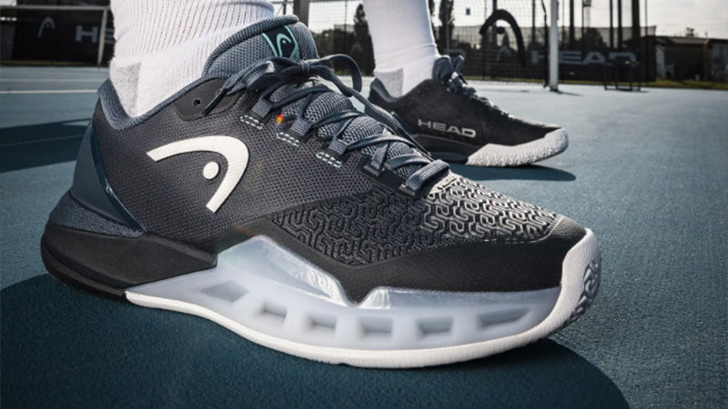 Closeup of a person wearing HEAD dark blue Revolt Pro 5.0 tennis shoes on a blue court