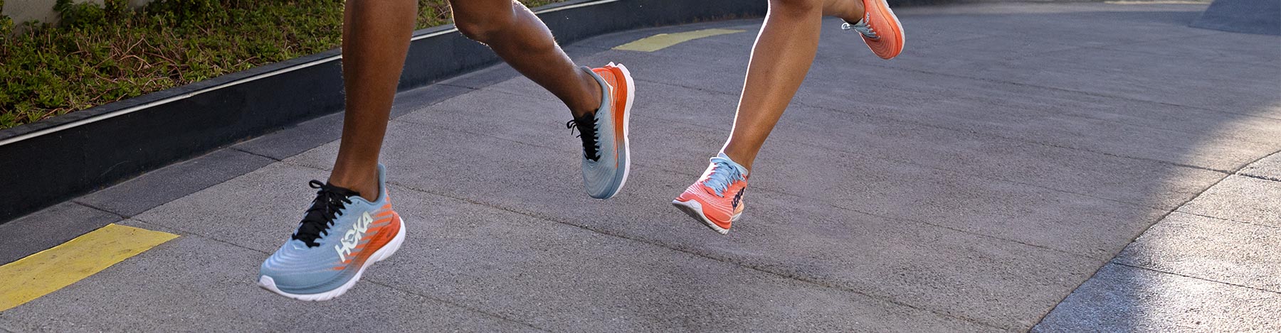 A man and a woman running on a sidewalk in HOKA Mach 5 running shoes.