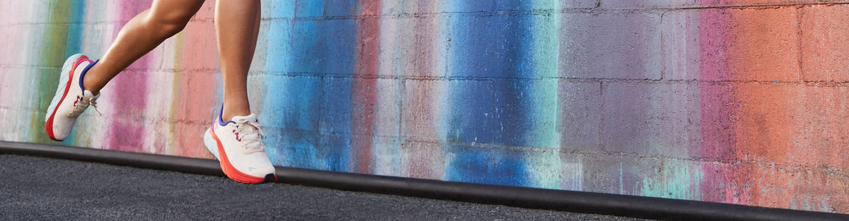 Women in front of rainbow colored wall wearing HOKA Arahi 6 Start Pack running shoes