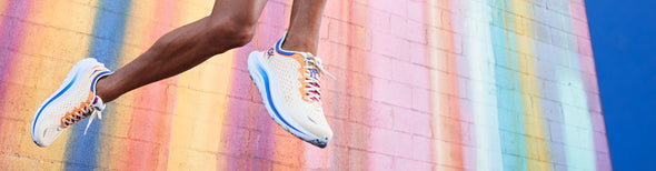 Man jumping in front of colorful wall wearing HOKA Kawana Start Pack running shoes