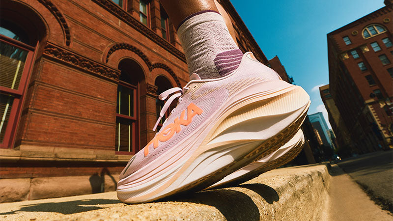 Person wearing pink HOKA Skyward X 2 women's running shoes with orange accents on a city street.