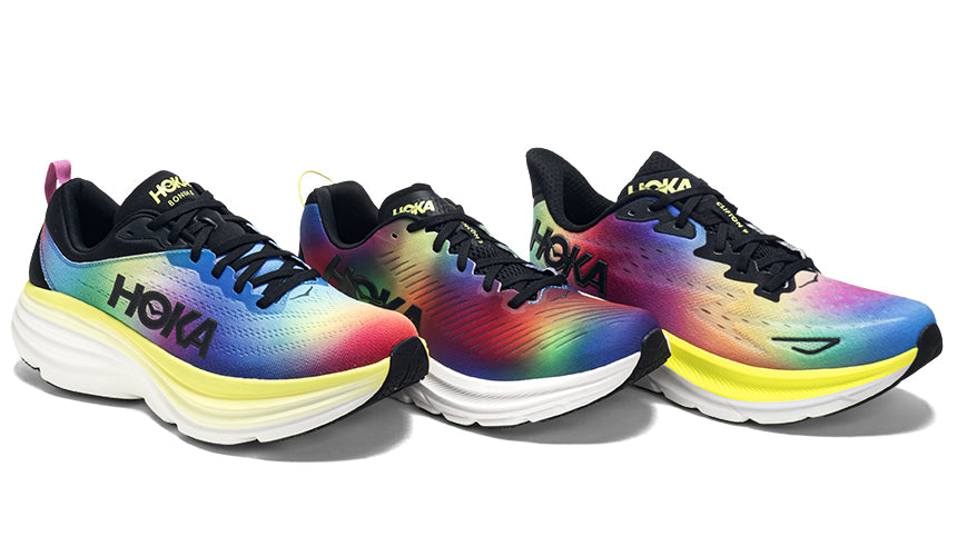 closeup of people standing in multi-colored HOKA running shoes on a paved surface.