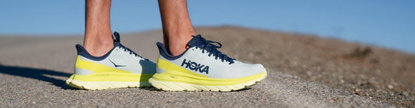 Man standing along a rural road wearing Hoka One One Mach 4 Blue Flower/Citrus running shoes.