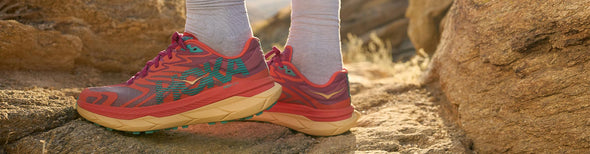 Close up of a person standing in orange HOKA Tecton X 2 trail running shoes on a desert rock.