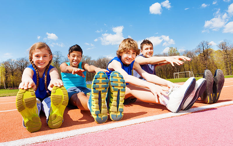Smiling kids stretching in running shoes on track
