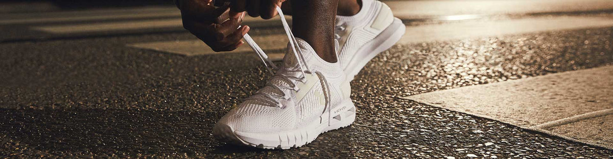Man in white Under Armour running shoes tying up laces