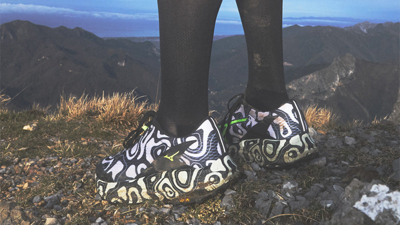 a person standing on a mountain trail wearing black and white Mizuno Neo Accera trail running shoes