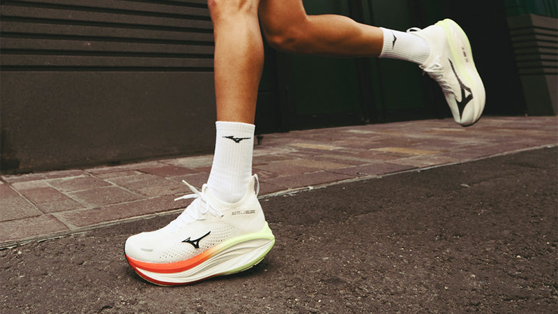 A person running on a paved road along a brick sidewalk in white, red and yellow Mizuno Neo Vista 3 running shoes 