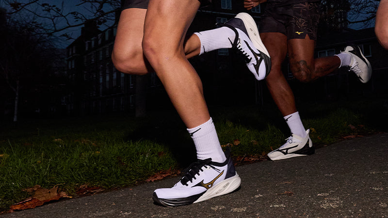 People running on a college campus at night in Mizuno Origami collection black, white and gold running shoes