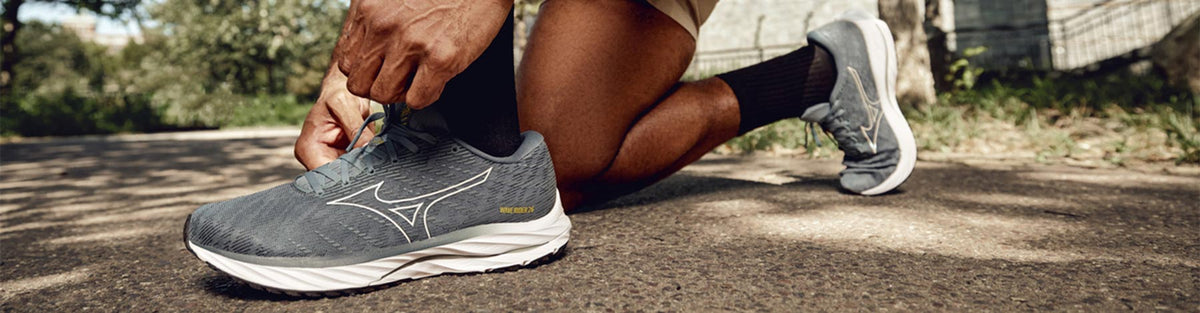 A runner leaning to tie their gray Mizuno Wave Rider 26 running shoes.