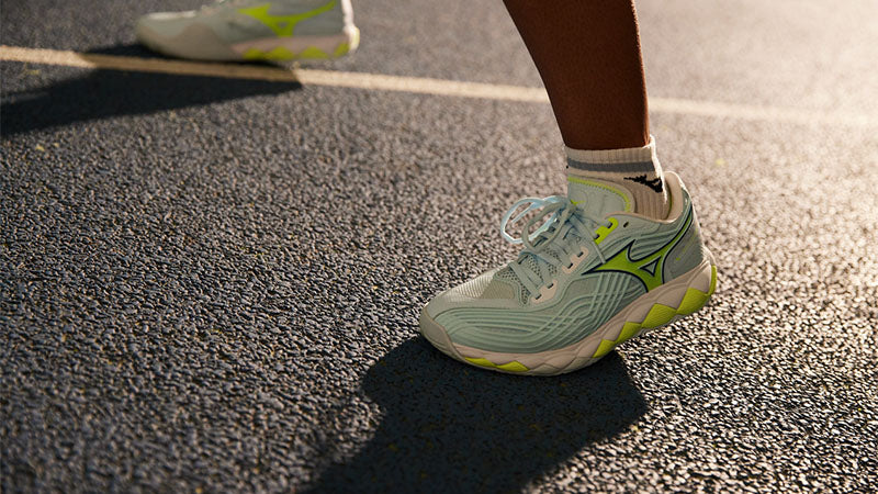 Closeup of a tennis player wearing Mizuno Wave Enforce Tour 2 AC shoes on a hard court surface