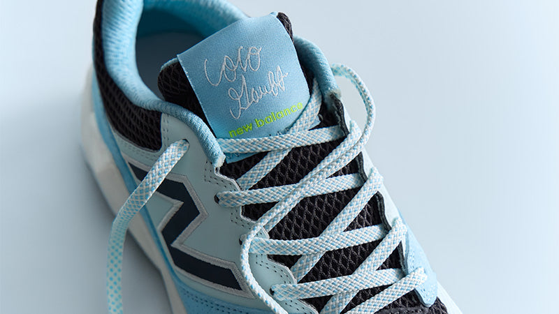 closeup of a blue New Balance FuelCell Coco Delray tennis shoe on a light blue background