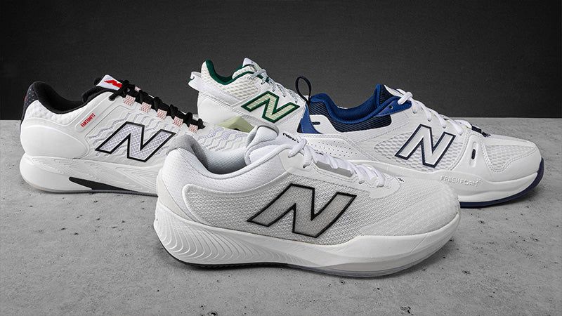 Four New Balance tennis shoes in different colors on a gray surface with a black background.