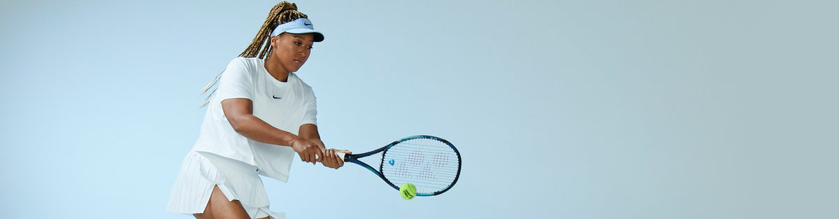 Naomi Osaka hitting a tennis ball with a Yonex EZONE Sky Blue tennis racquet dressed in Nike tennis clothing against a light blue background.