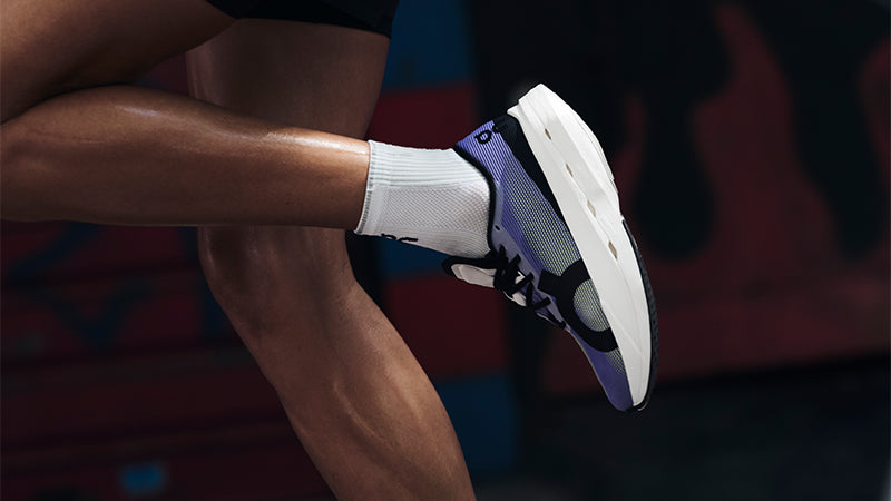 A person running in purple On Cloudboom Volt shoes with blurred street art in the background
