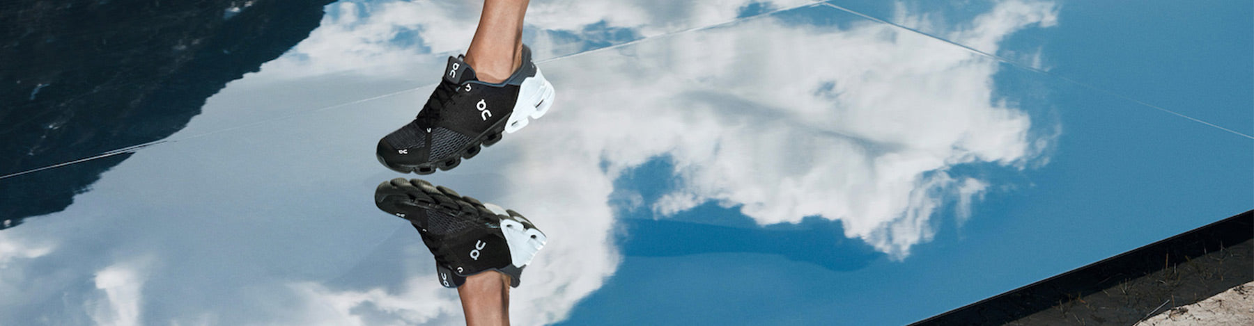 Man running in black and white On Cloudflyer running shoes on a reflective surface showing a blue sky with white clouds.
