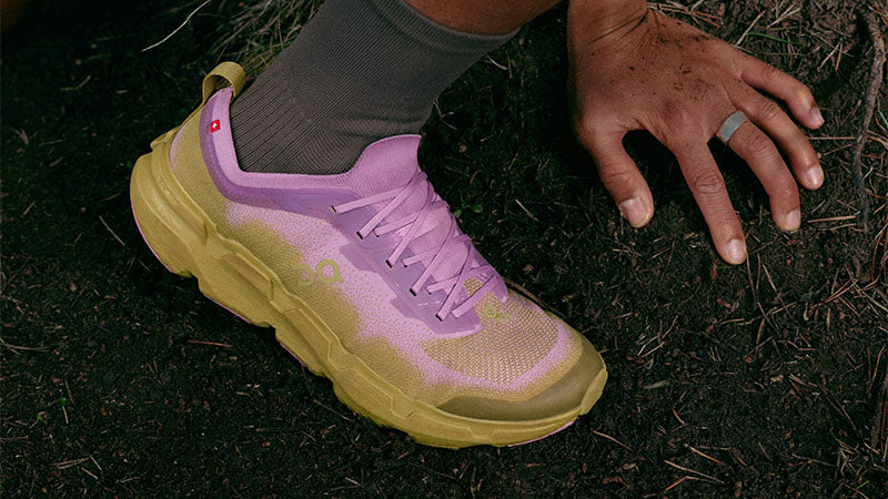 Closeup of a trail runner on a dirt path wearing pink and khaki On Cloudsoma men's trail running shoes