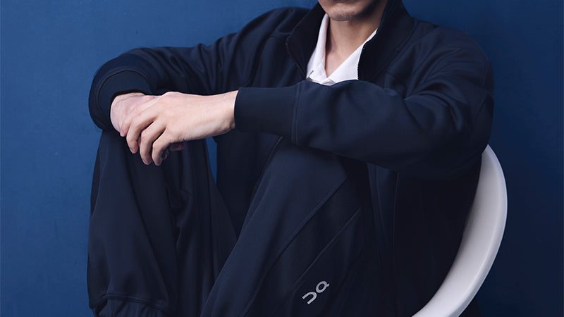 Person wearing a dark blue tennis outfit with a white 'On' logo on a blue background