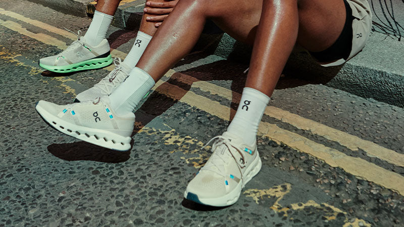 Two runners sitting on a roadside curb wearing On Cloudsurfer 2 running shoes