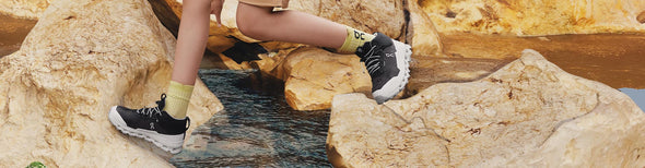 a child running across a rocky stream in black and white On Cloudhero Mid Waterproof Junior hiking shoes
