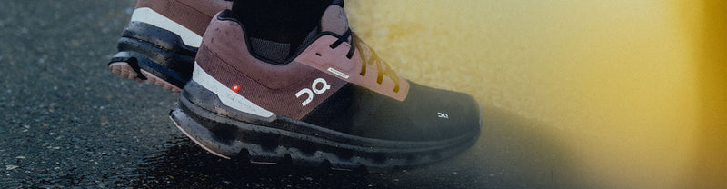 Closeup of a person wearing On Cloudrunner Waterproof running shoes on a wet pavement.