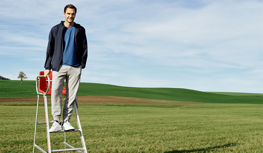roger federer wearing on the roger advantage tennis shoes while standing on a tennis umpire chair in a green field
