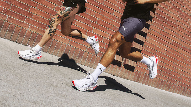 Two runners on a sidewalk wearing Puma Deviate Pure NITRO shoes with a brick wall in the background