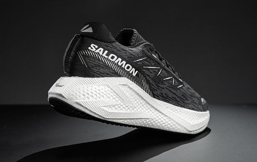 Person wearing white Salomon Aero Glide 4 running shoes with black socks on a white background