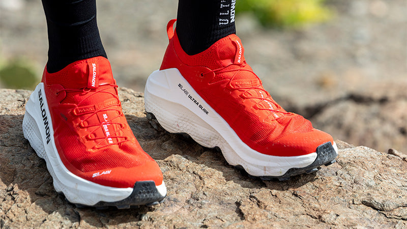 person standing on a rocky surface wearing red and white Salmon S/Lab Ultra Glide 2 Unisex trail running shoes