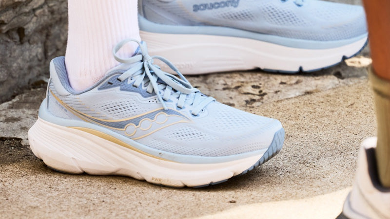Light blue Saucony Guide 19 running shoes with a white midsole and gold accents worn by a person standing on a stone surface