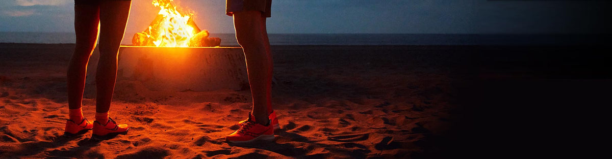 Two people standing next to a beach campfire in Saucony Campfire Stories running and trail running shoes.