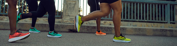 Group running along a paved bridge in orange, yellow and mint colored Saucony Guide 15 running shoes.