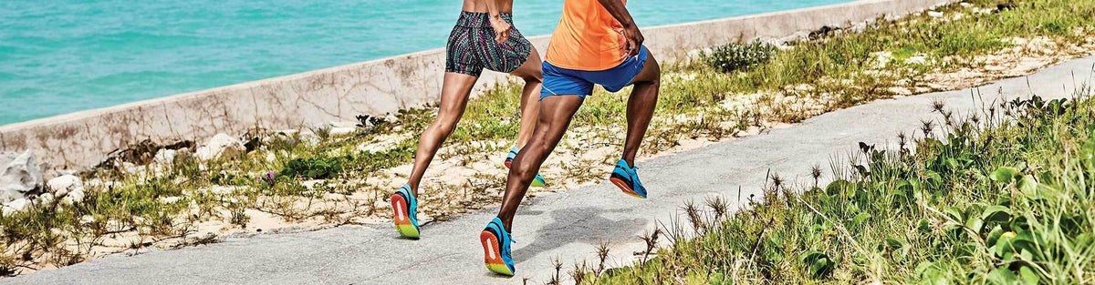 Man and woman running by the ocean in Saucony running shoes and athleticwear