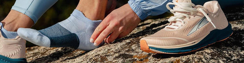 Lifestyle image: Closeup of a trail runner sitting on a rock wearing Feetures socks.