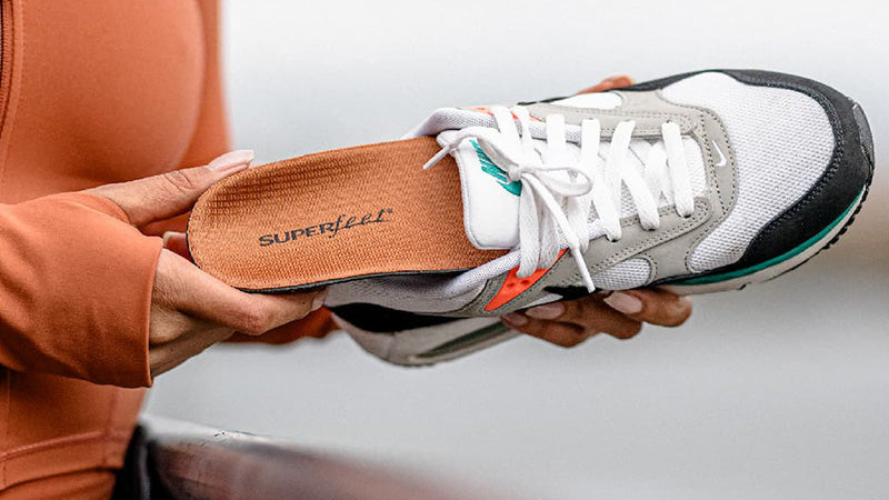 A person holding up a running shoe with a Superfeet All-Purpose Memory Foam Support insole