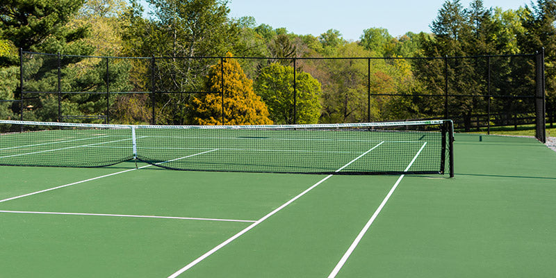 A green tennis court with forest trees and a blue sky in the background